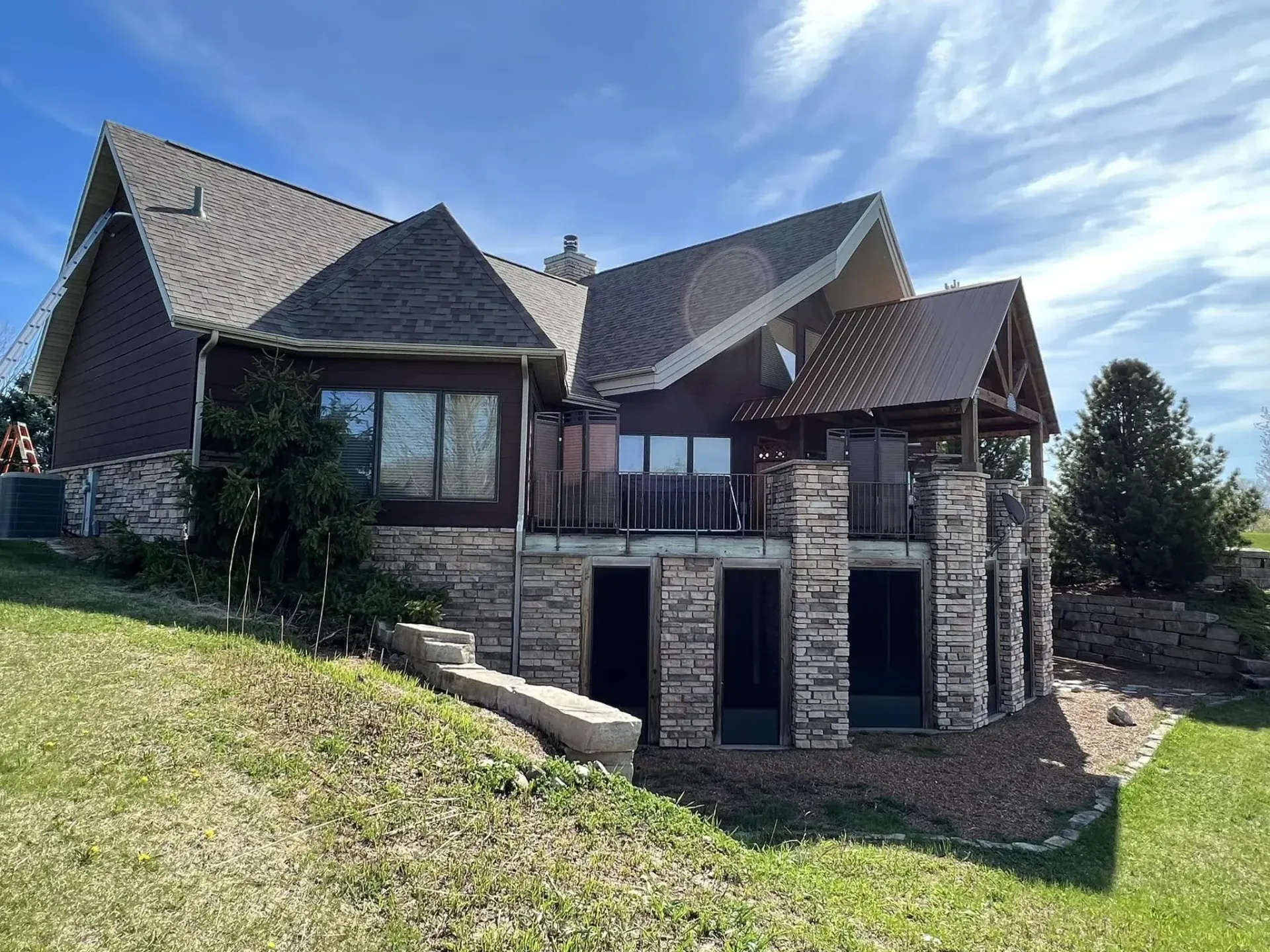 Stone house with dark roofs and a large front porch on a sunny grassy hillside