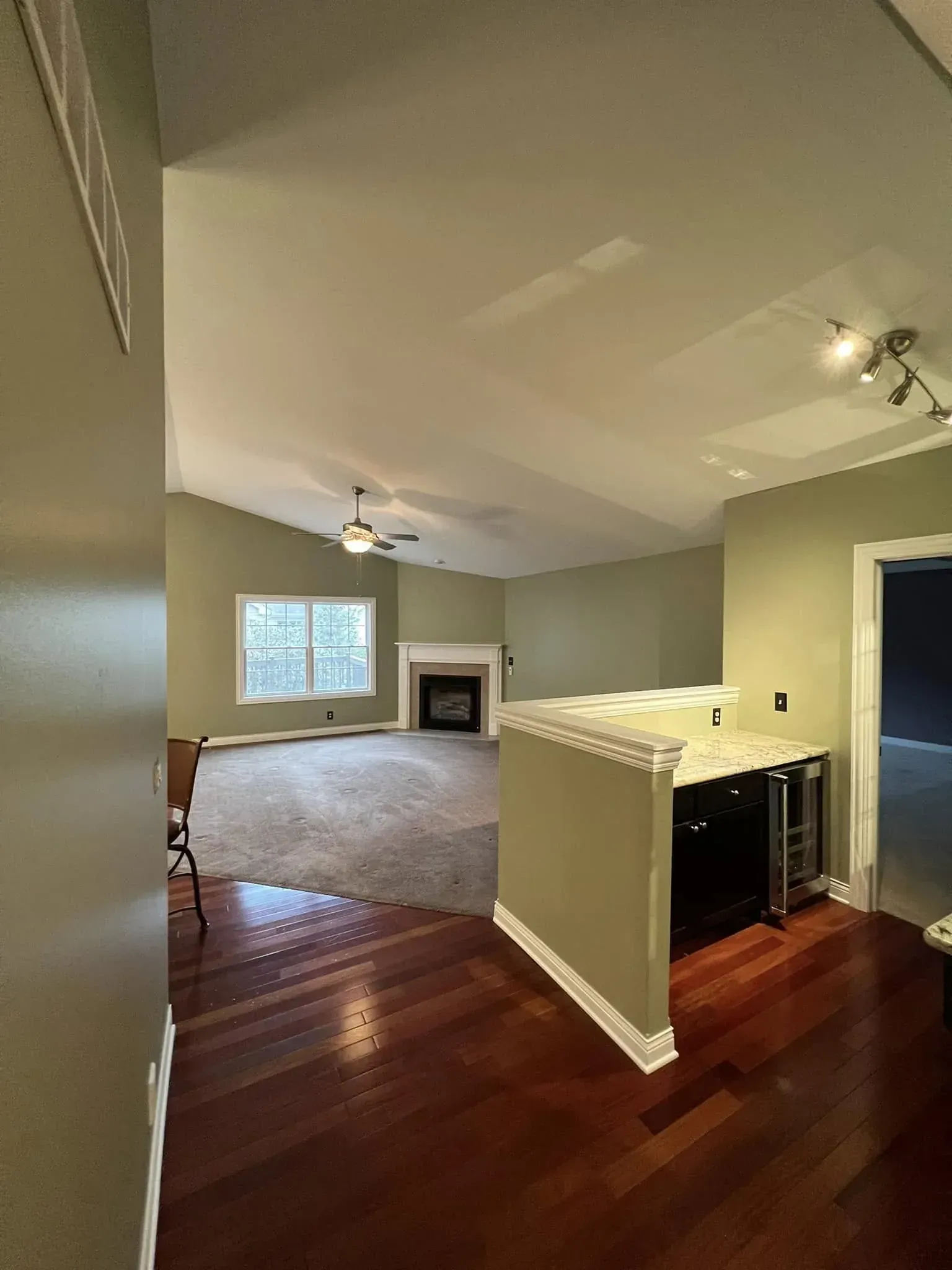 Open-concept living room with hardwood floors, carpeted area, ceiling fans, window, and fireplace.