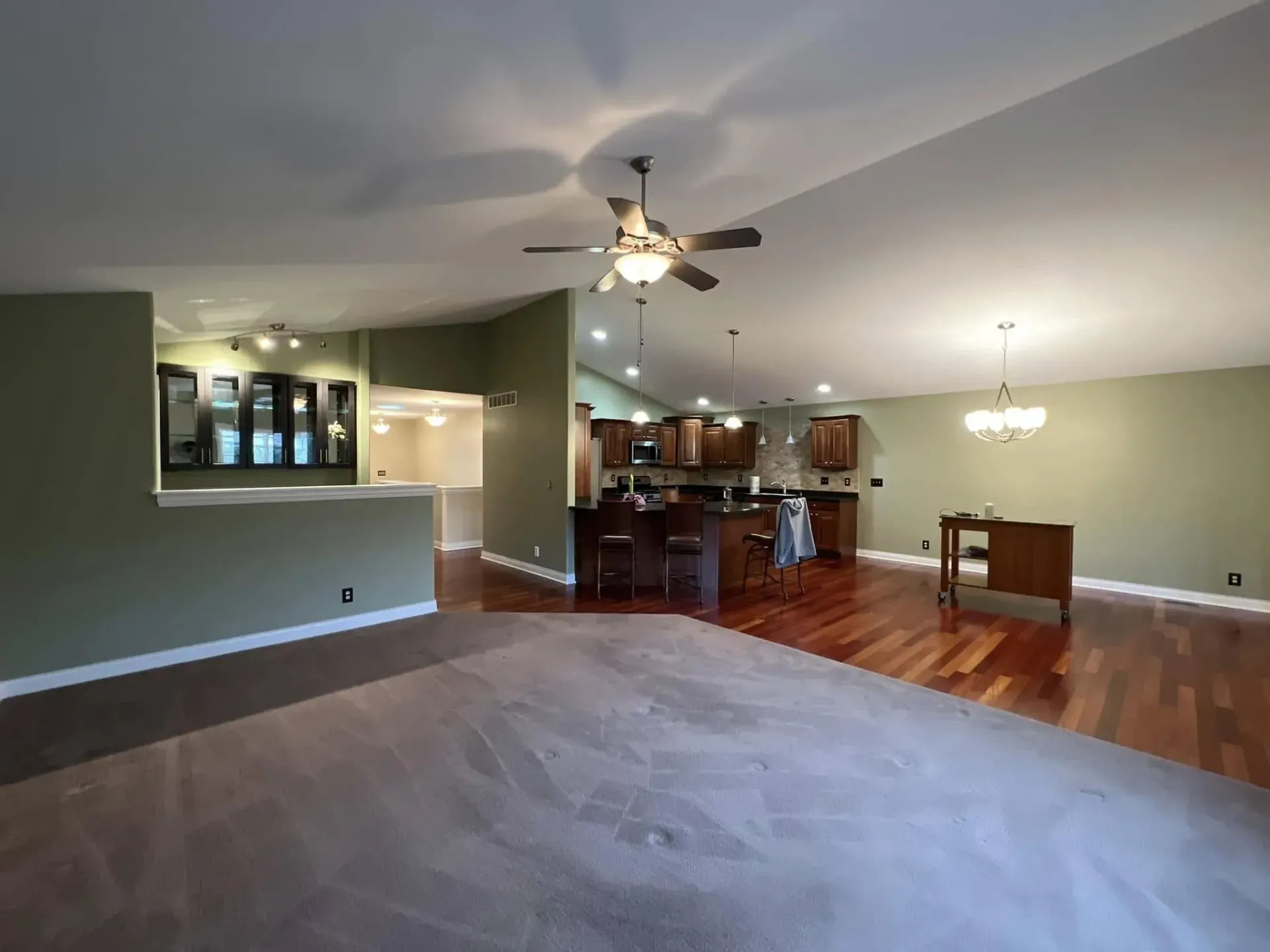 Empty living room and kitchen with hardwood floors, green walls, ceiling fans, and a dining table.