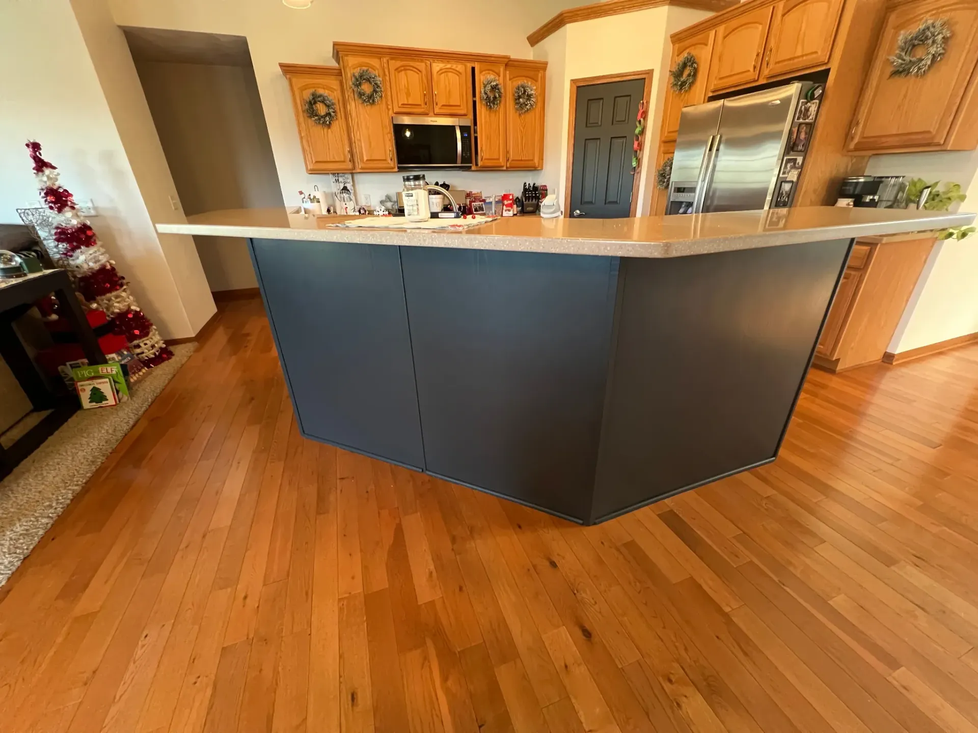 Kitchen with wood cabinets, granite island, hardwood floor, and a stainless steel refrigerator.