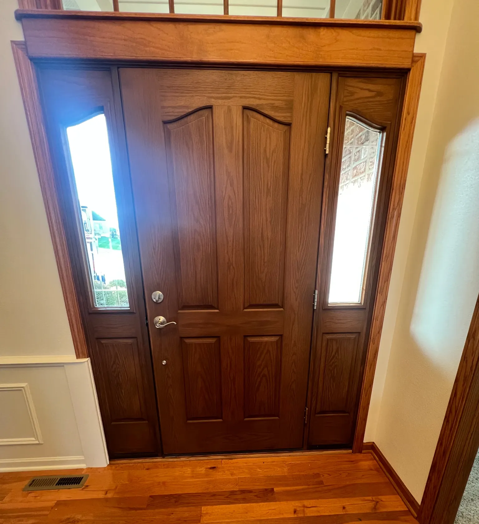 Wooden front door with two narrow glass side panels in a hallway with hardwood floor