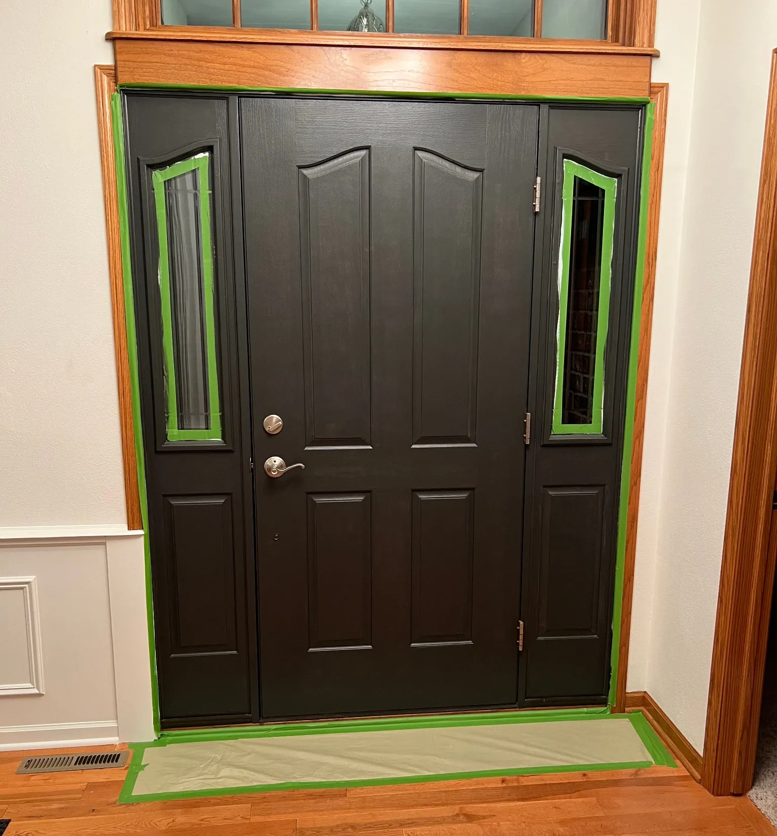Black front door with narrow green-trimmed sidelights and a gray doormat inside a home entryway