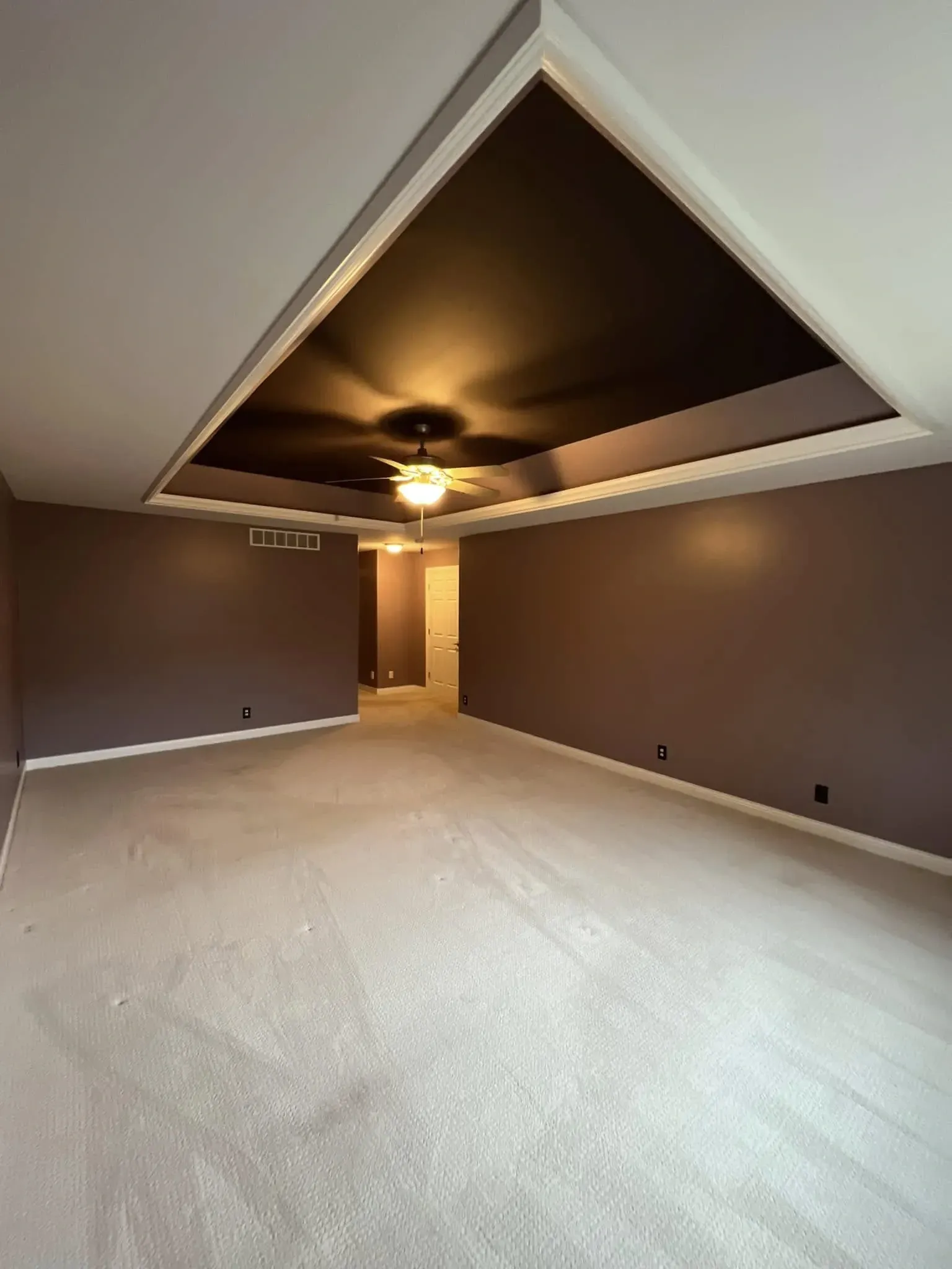 Empty carpeted room with brown walls, vaulted ceiling, and a ceiling fan lit in the center