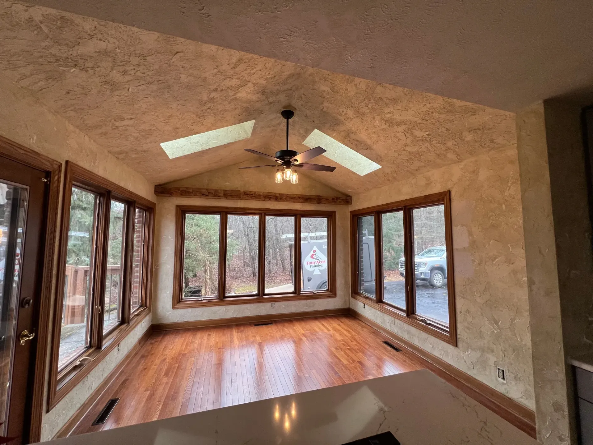 Empty sunroom with wood floors, many windows, and a ceiling fan under a textured ceiling.