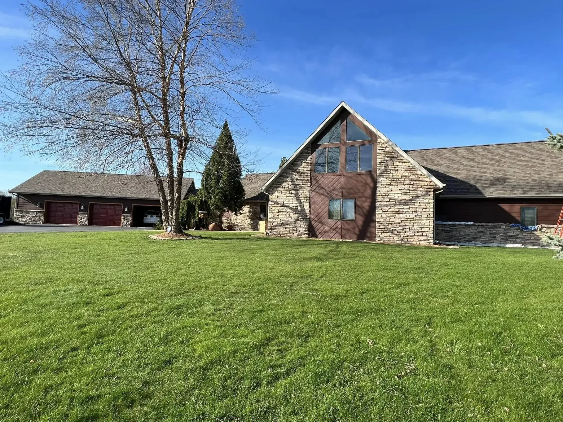 Stone suburban house with a large green lawn and blue sky