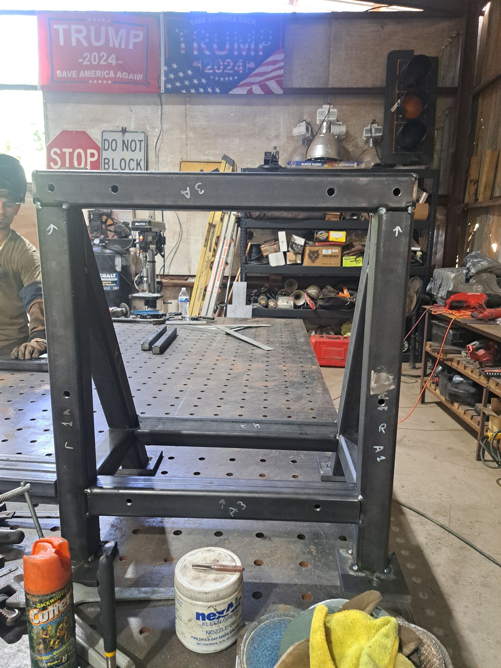 Welding table frame under construction in a workshop; Trump signs in the background.