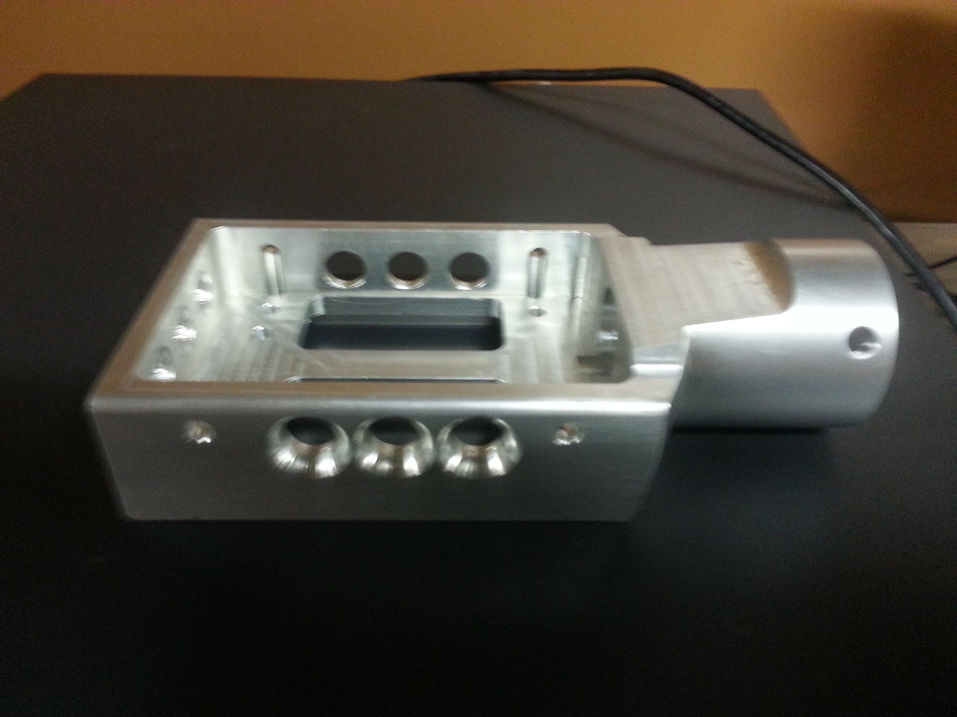Aluminum machined part with several holes and a cylindrical extension.
