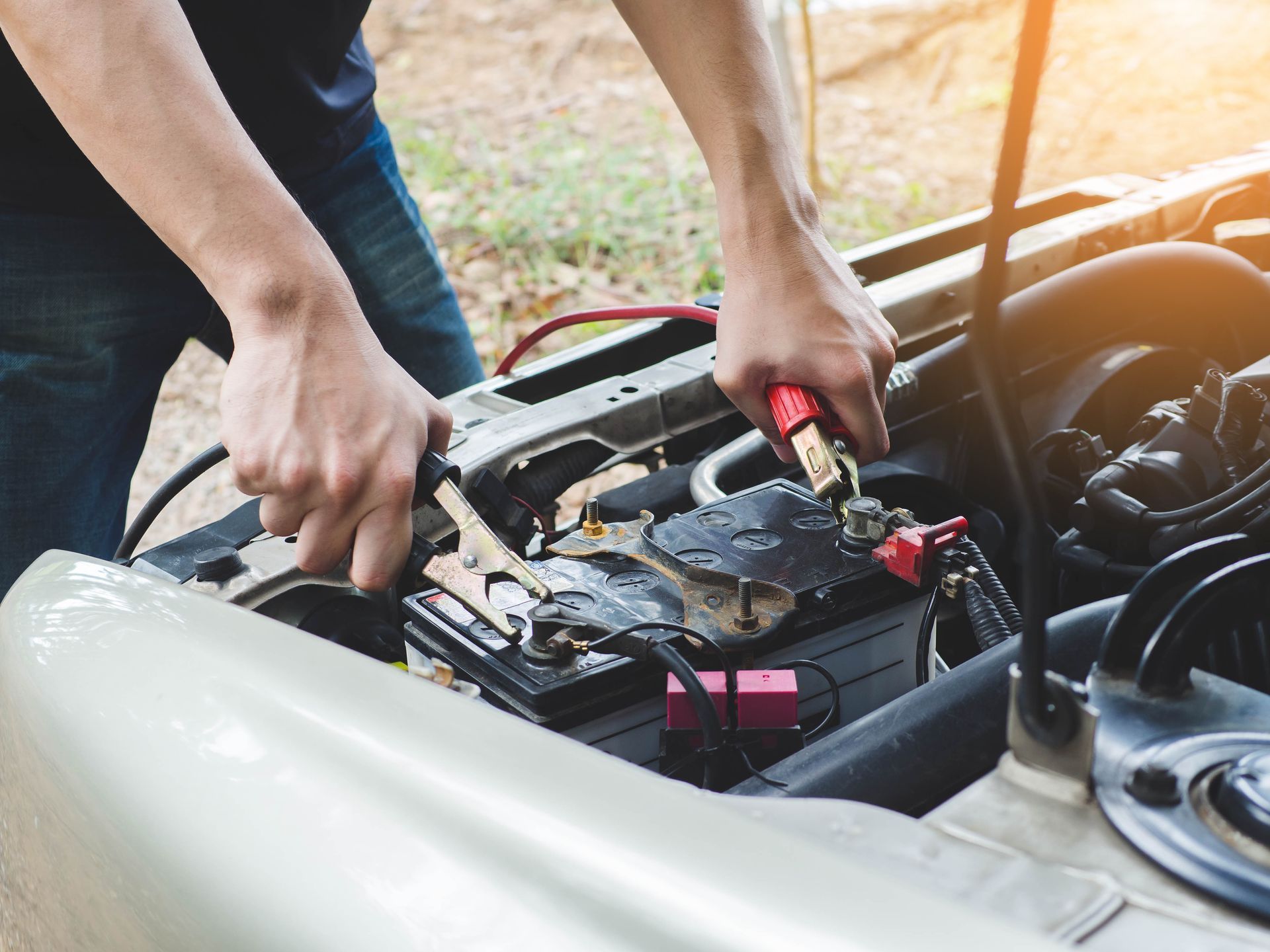 Hands using jumper cables to jump-start a car battery in an open engine bay | Ron's Auto & RV