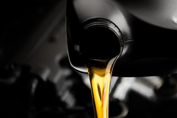 Golden oil pouring from a car engine oil filler spout against a dark background