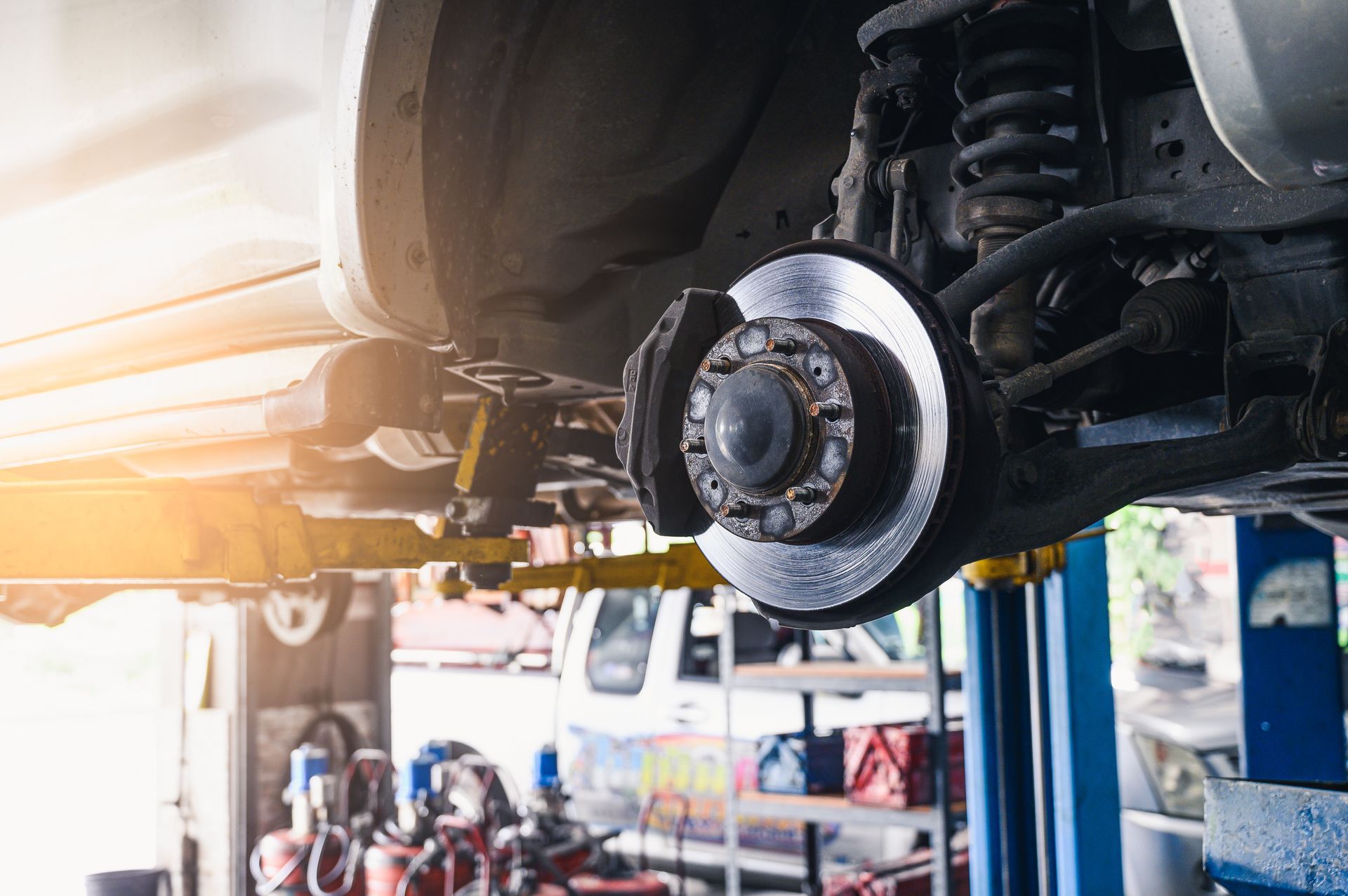 Car lifted on a repair hoist in an auto shop, showing the front wheel and brake assembly. | Ron's Auto & RV