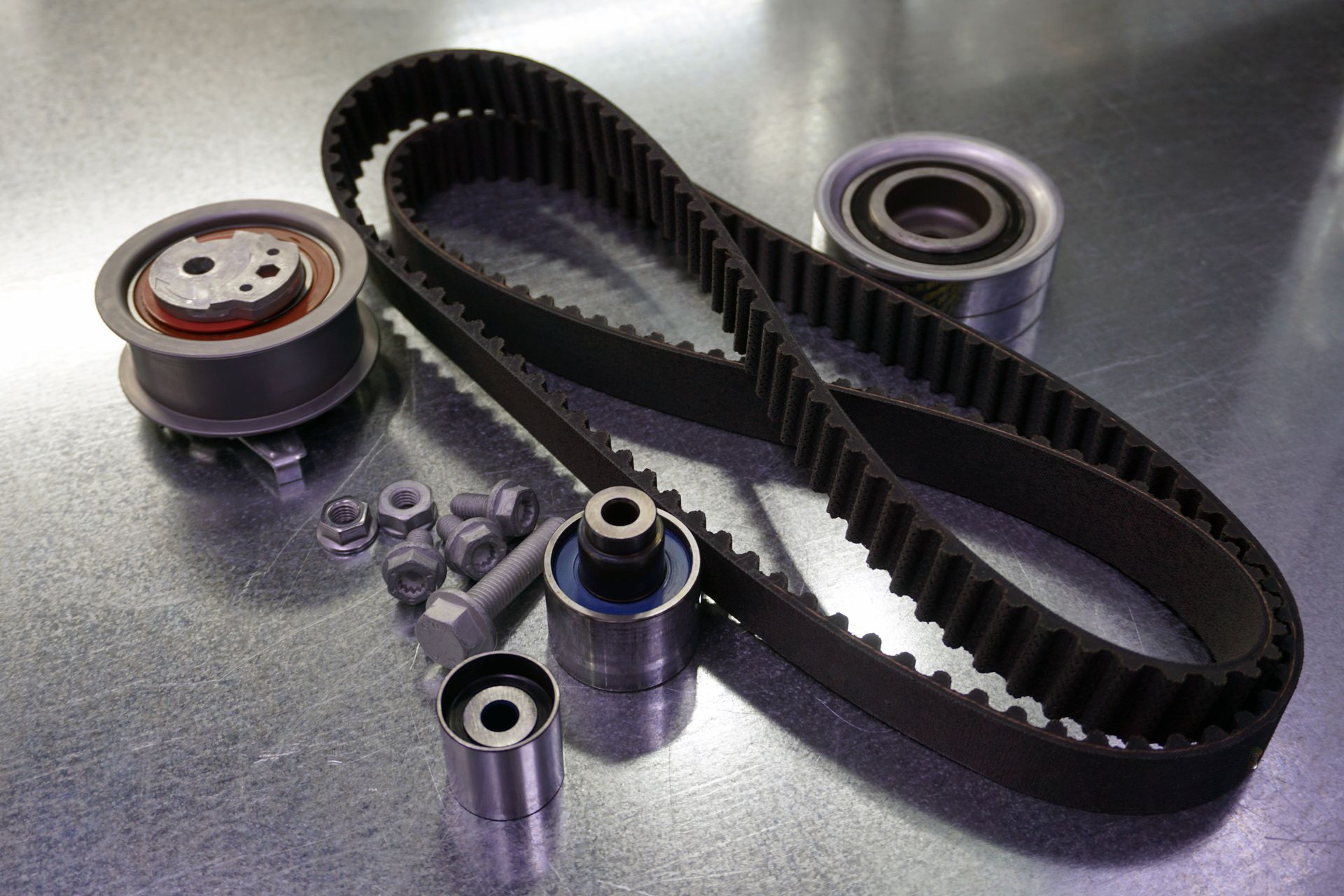 Black timing belt with metal pulleys, bearings, and small hardware on a reflective surface | Ron's Auto & RV