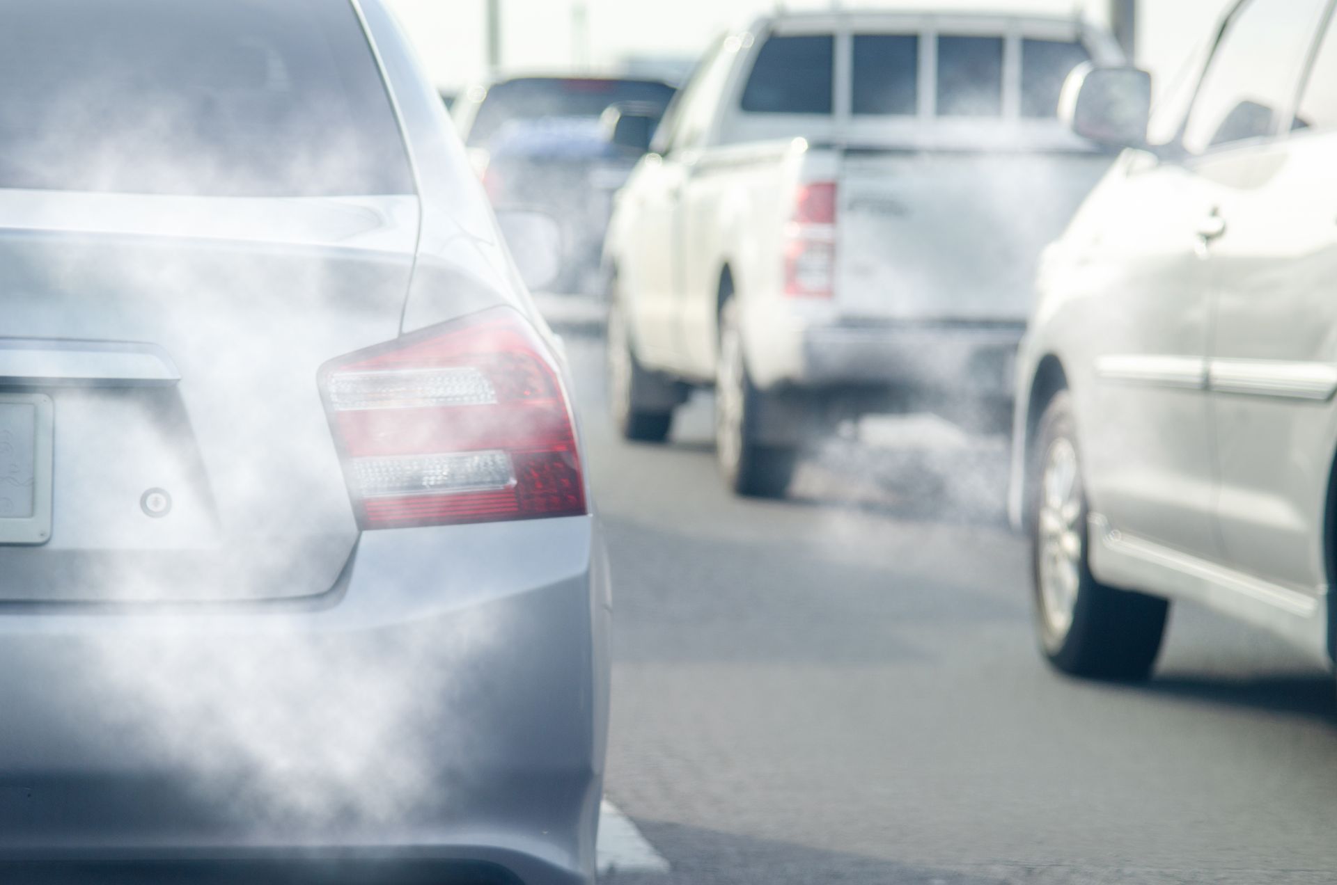 Cars in traffic with visible exhaust smoke on a roadway | Ron's Auto & RV