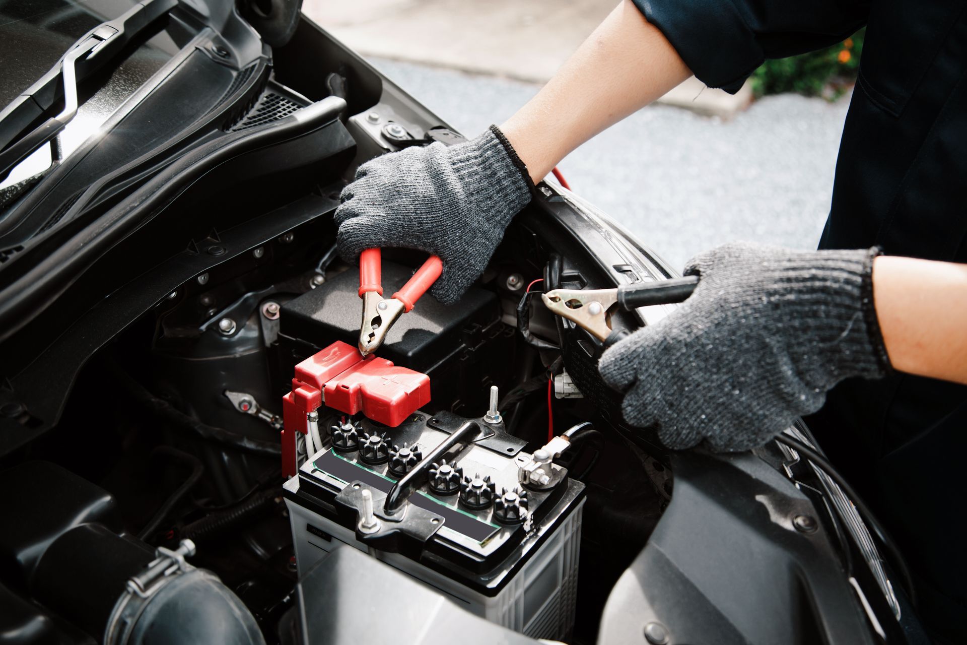 Gloved hands jump-starting a car battery with red and black cables under the hood | Ron's Auto & RV