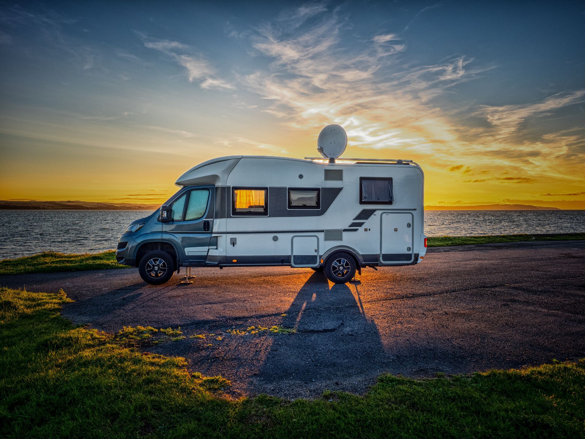 Camper van parked by the water at sunset, with warm sky reflections and a satellite dish on top | Ron's Auto & RV