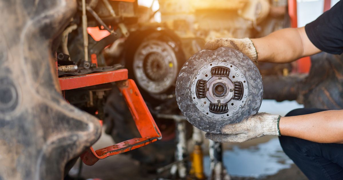 Mechanic holding a brake rotor in a garage, with a wheel hub and tools in the background | Ron's Auto & RV