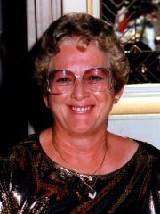 Smiling person with short curly hair and glasses, wearing a dark patterned top indoors. | Ron's Auto & RV