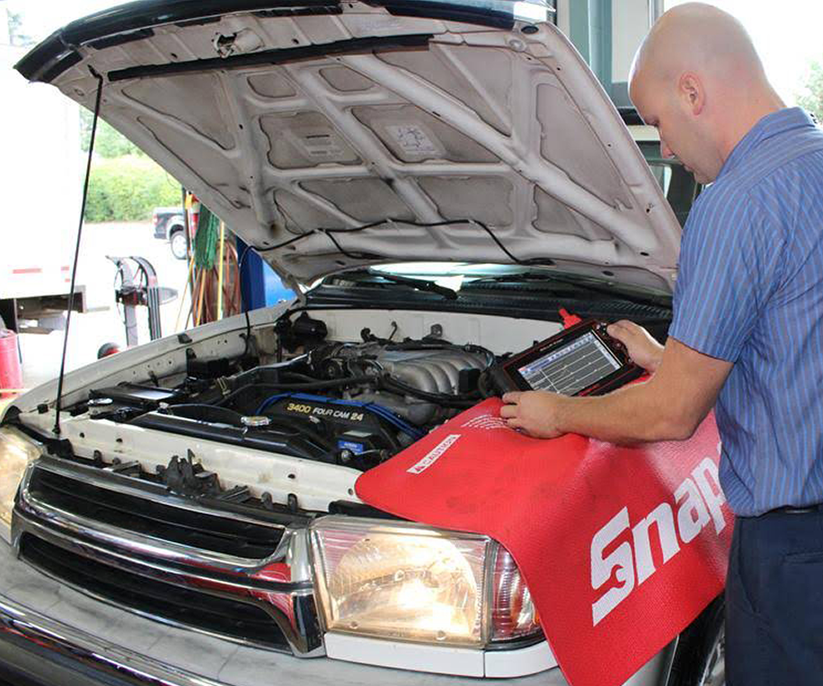 Mechanic checking a car engine under the open hood with a red Snap-on tool mat