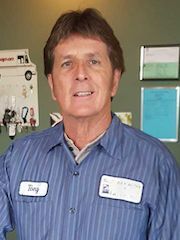 Man in blue striped shirt with name tag standing indoors against a bulletin board. | Ron's Auto & RV