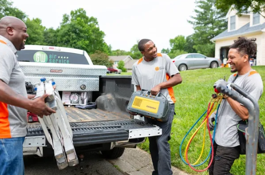 Three workers unloading tools from a pickup truck in a driveway
