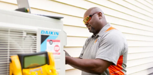 Technician inspecting an outdoor Daikin AC unit beside a house window