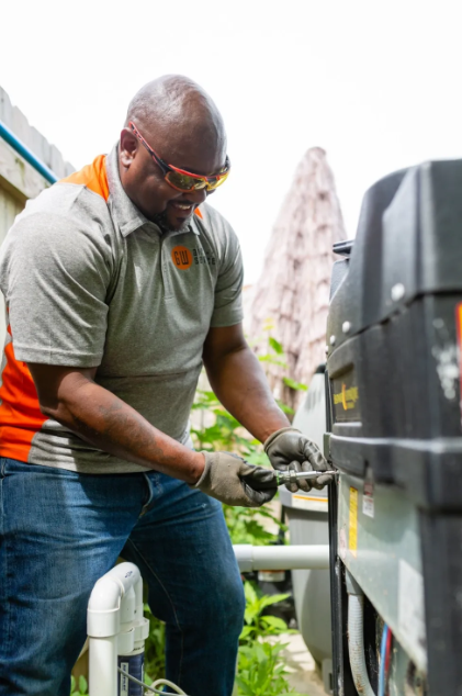 Worker in gray polo and gloves tightening bolts on outdoor equipment unit