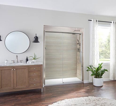 Modern bathroom with wood vanity, round mirror, glass shower door, and potted plant by the window