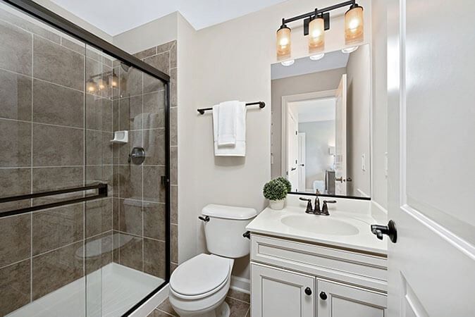 Modern bathroom with glass shower, white vanity, toilet, and wall mirror under vanity lights