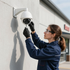 Technician adjusting a white security camera on an exterior wall of a building.