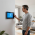 Man using a wall-mounted smart home touchscreen in a bright living room