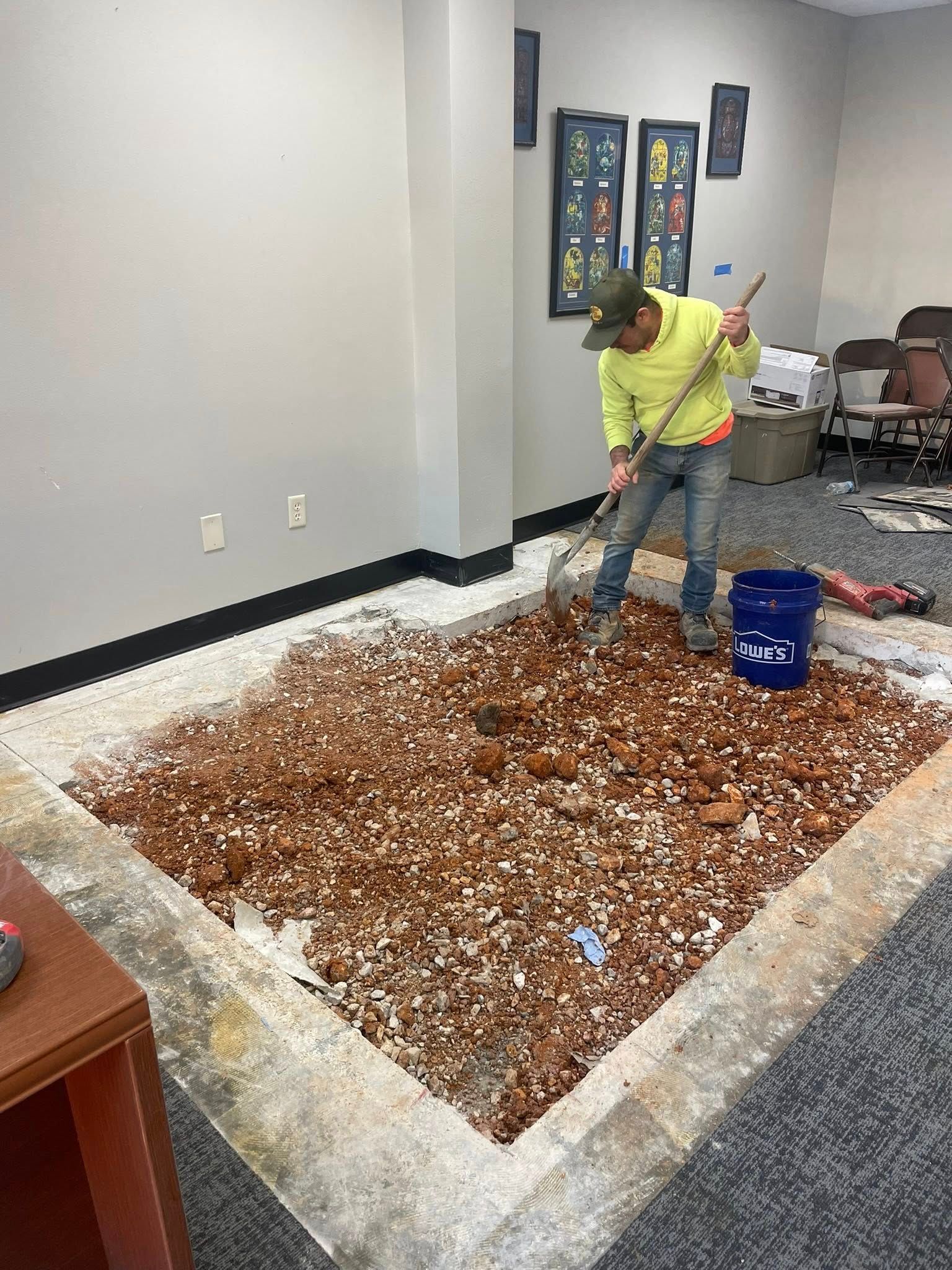 Person sweeping spilled debris off an office floor near a blue bin
