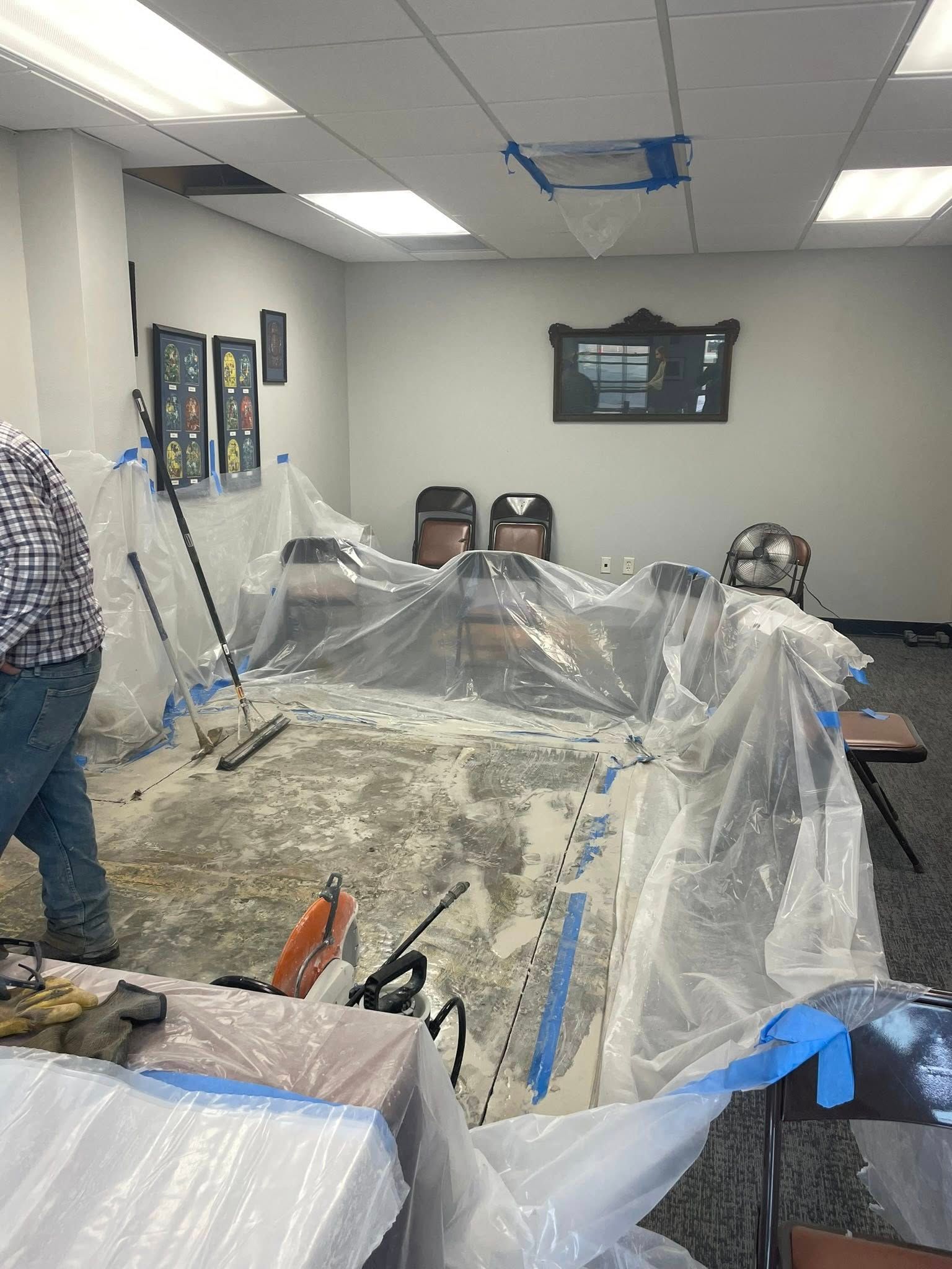 People doing a messy indoor renovation, with plastic sheeting covering furniture and tools on a table