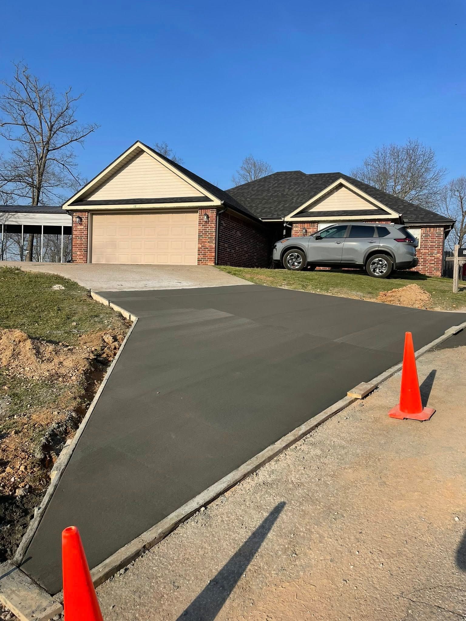 Driveway leading to two suburban garages, with a parked SUV and orange traffic cones on the roadside.