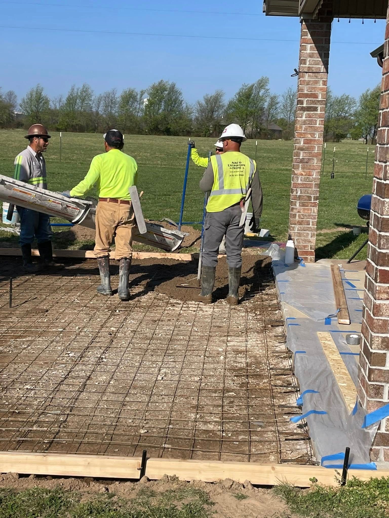 Workers pouring concrete over rebar at a construction site, with safety vests and formwork visible.