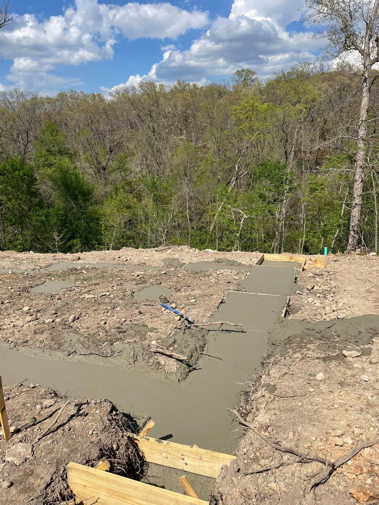 Concrete slab and rubble in a wooded area under a cloudy sky, with a narrow path leading into the trees