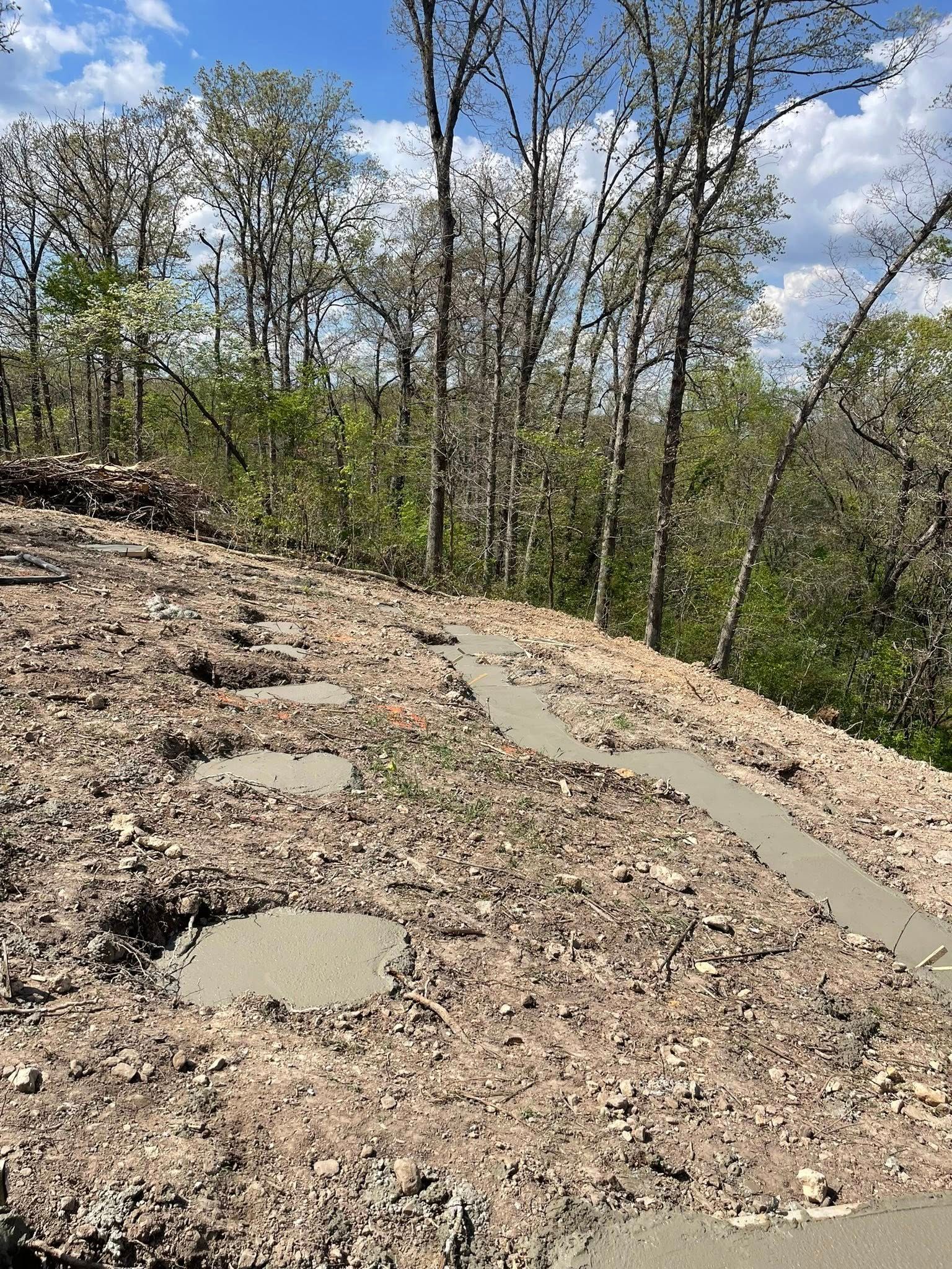 Rocky hillside trail with fresh concrete path sections under a partly cloudy sky