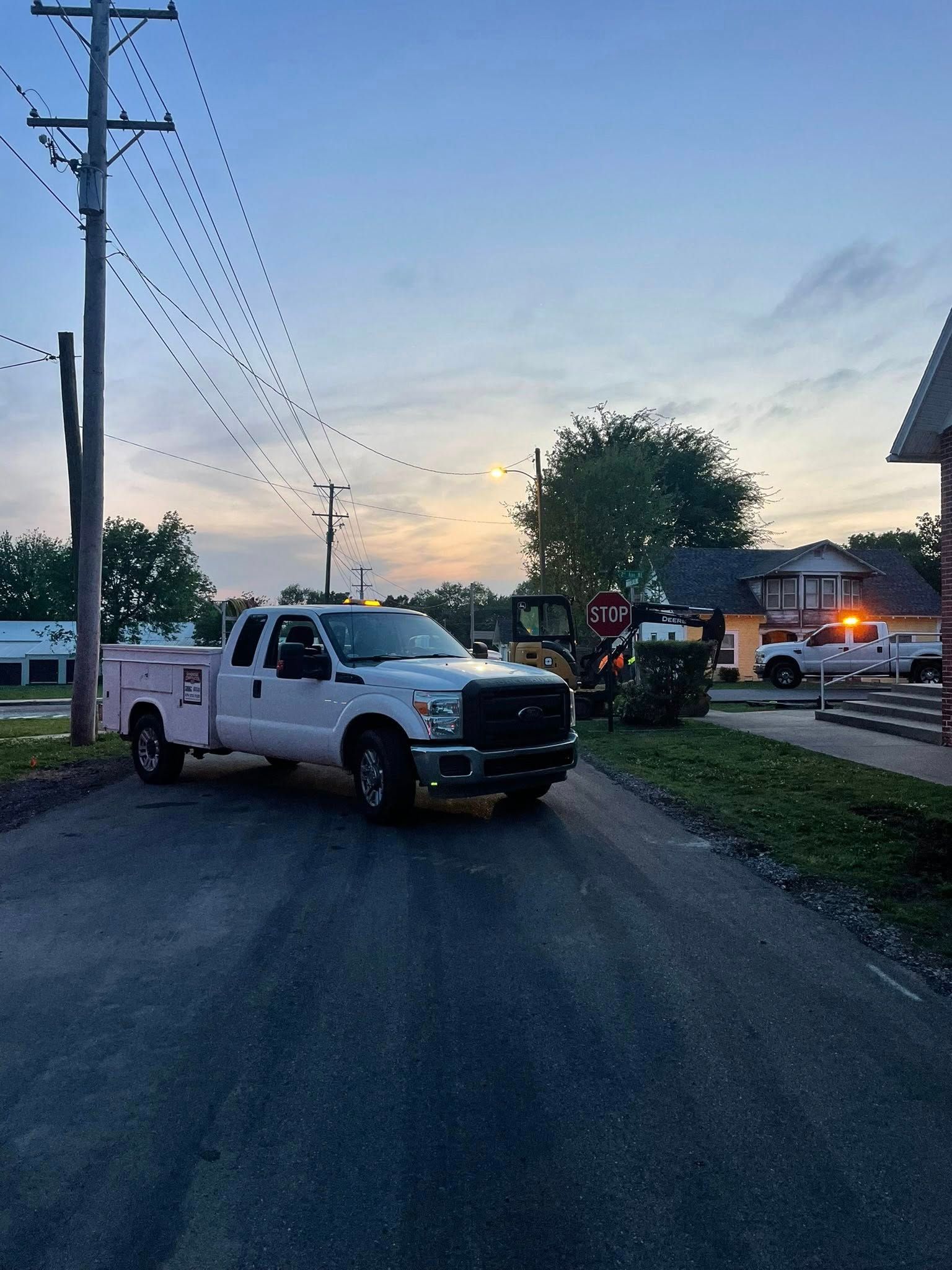 White pickup truck with trailer parked on a gravel road at dusk, near utility poles and houses.