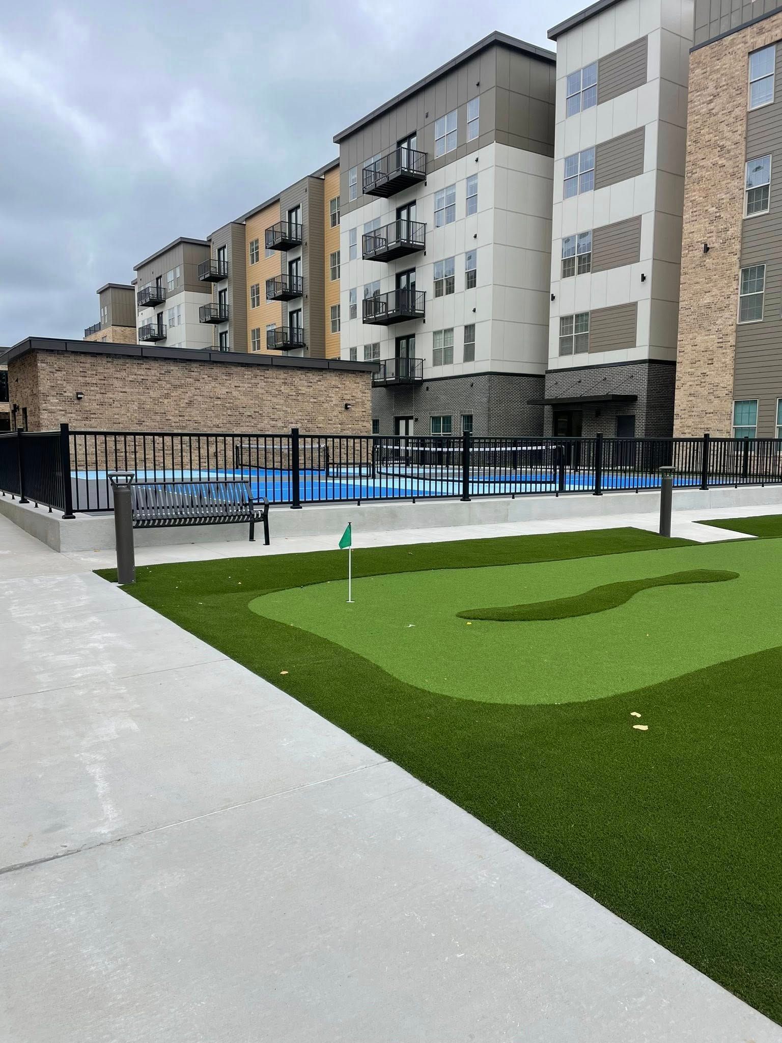 Modern apartment courtyard with turf, pool, and row of buildings under a cloudy sky
