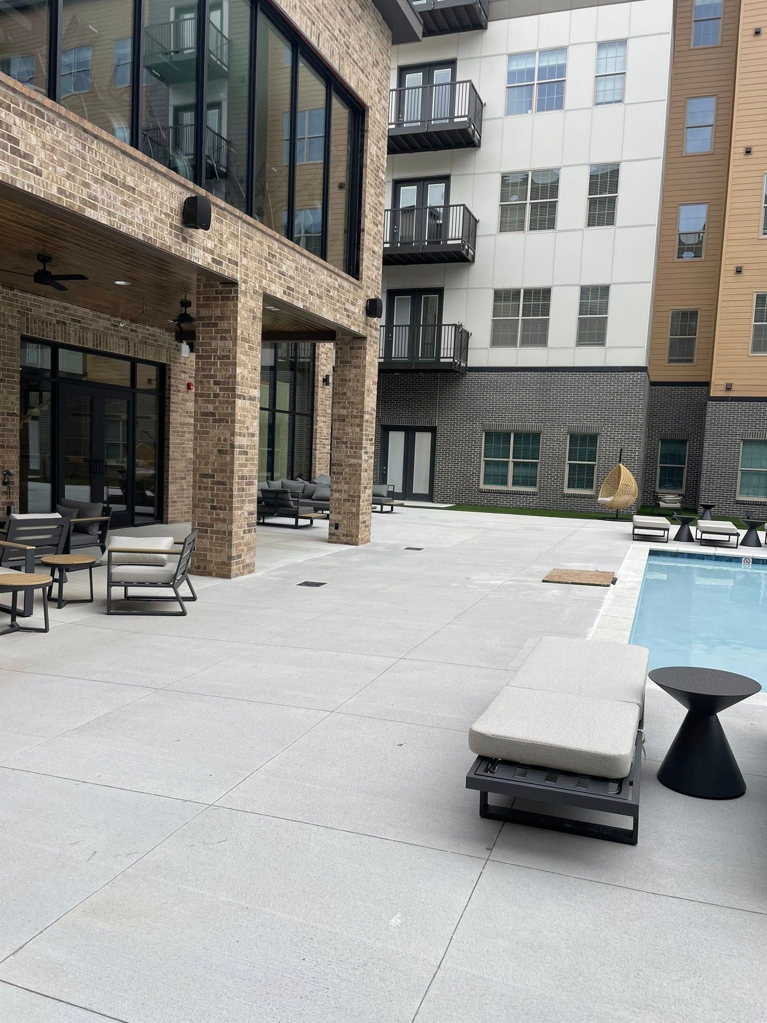 Modern apartment courtyard with stone buildings, seating, and a poolside area under construction.