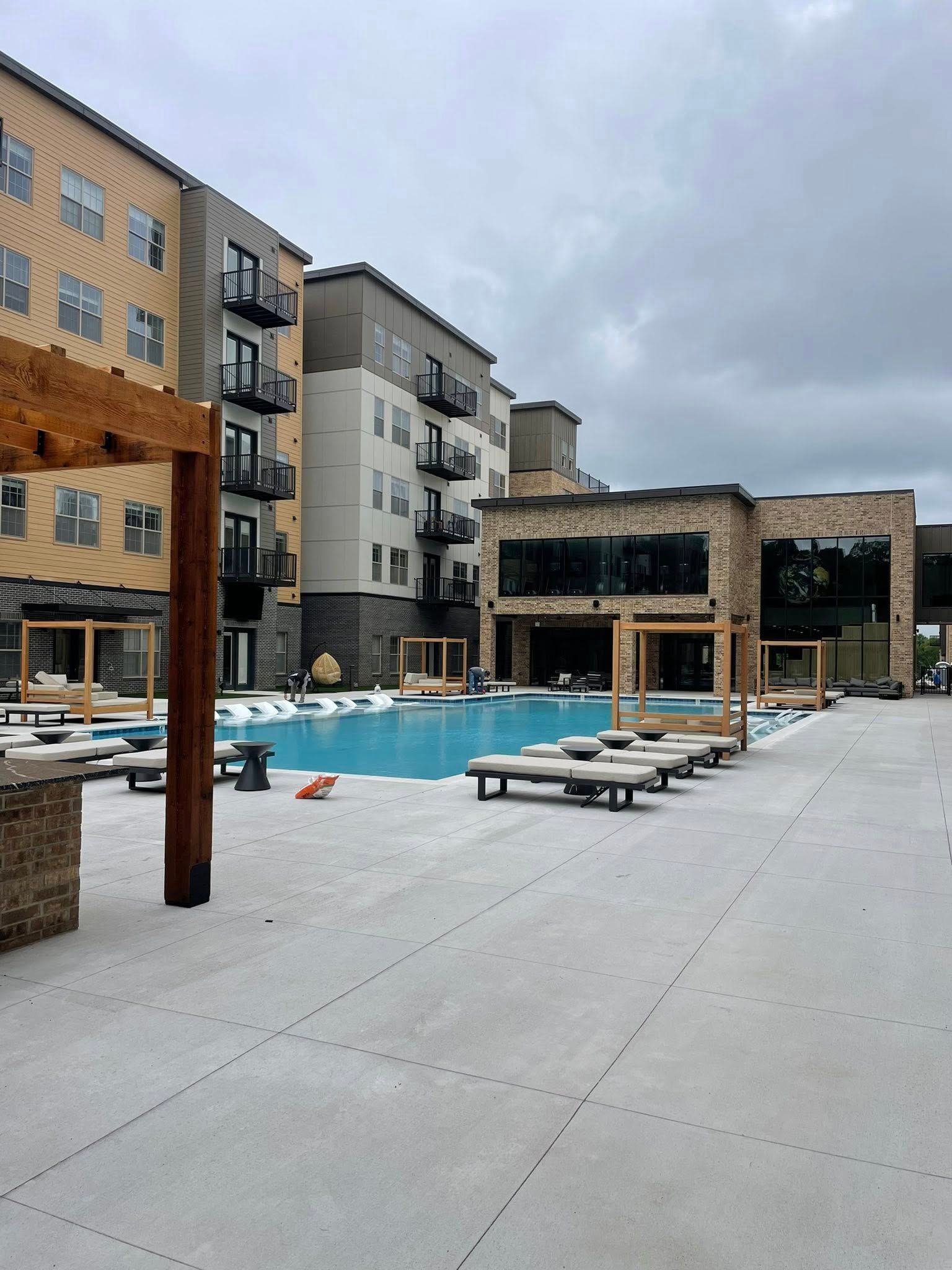 Outdoor hotel pool with lounge chairs and apartment buildings under a cloudy sky