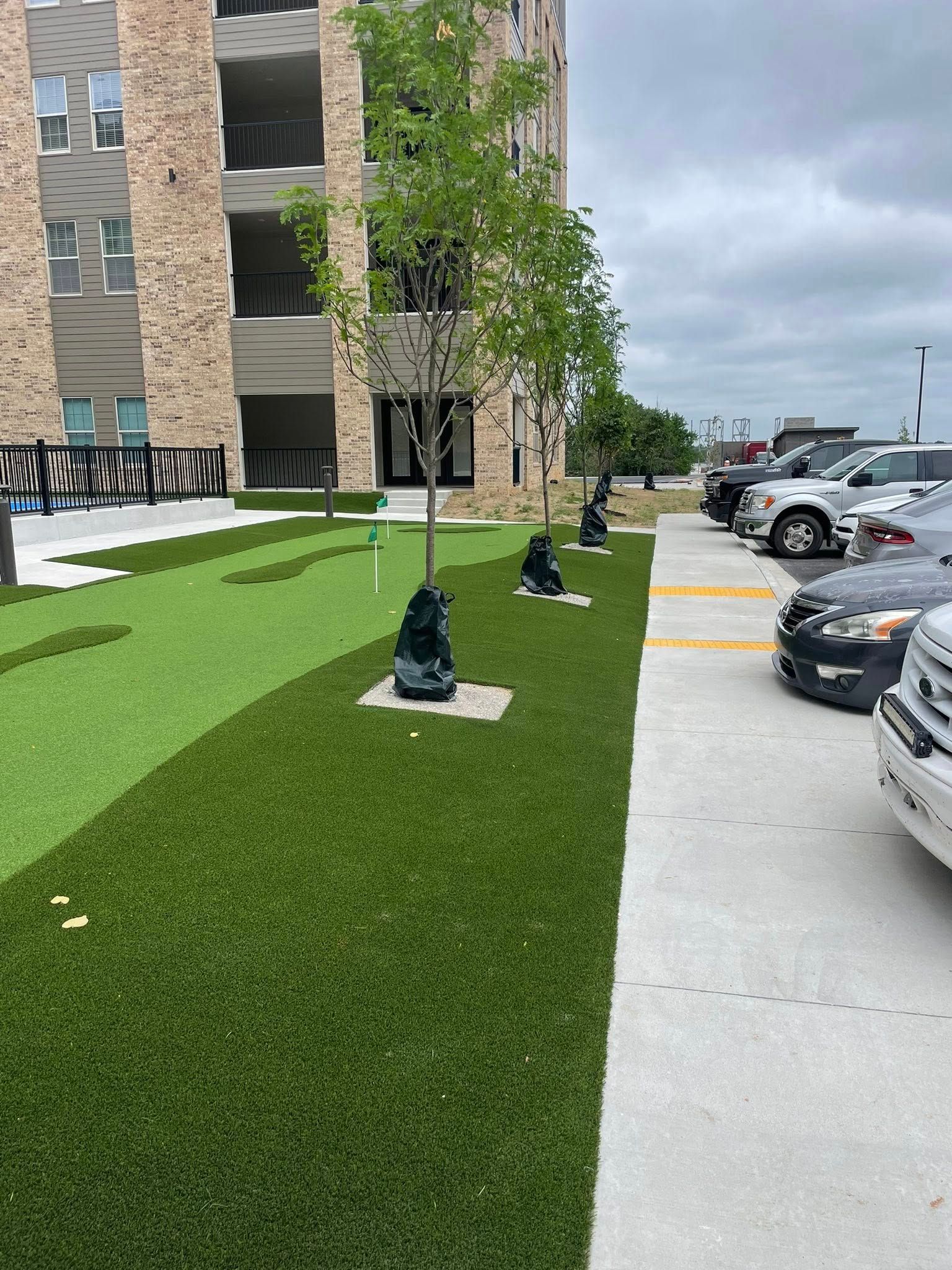 Apartment building with walkway, parking lot, and green landscaping under a cloudy sky