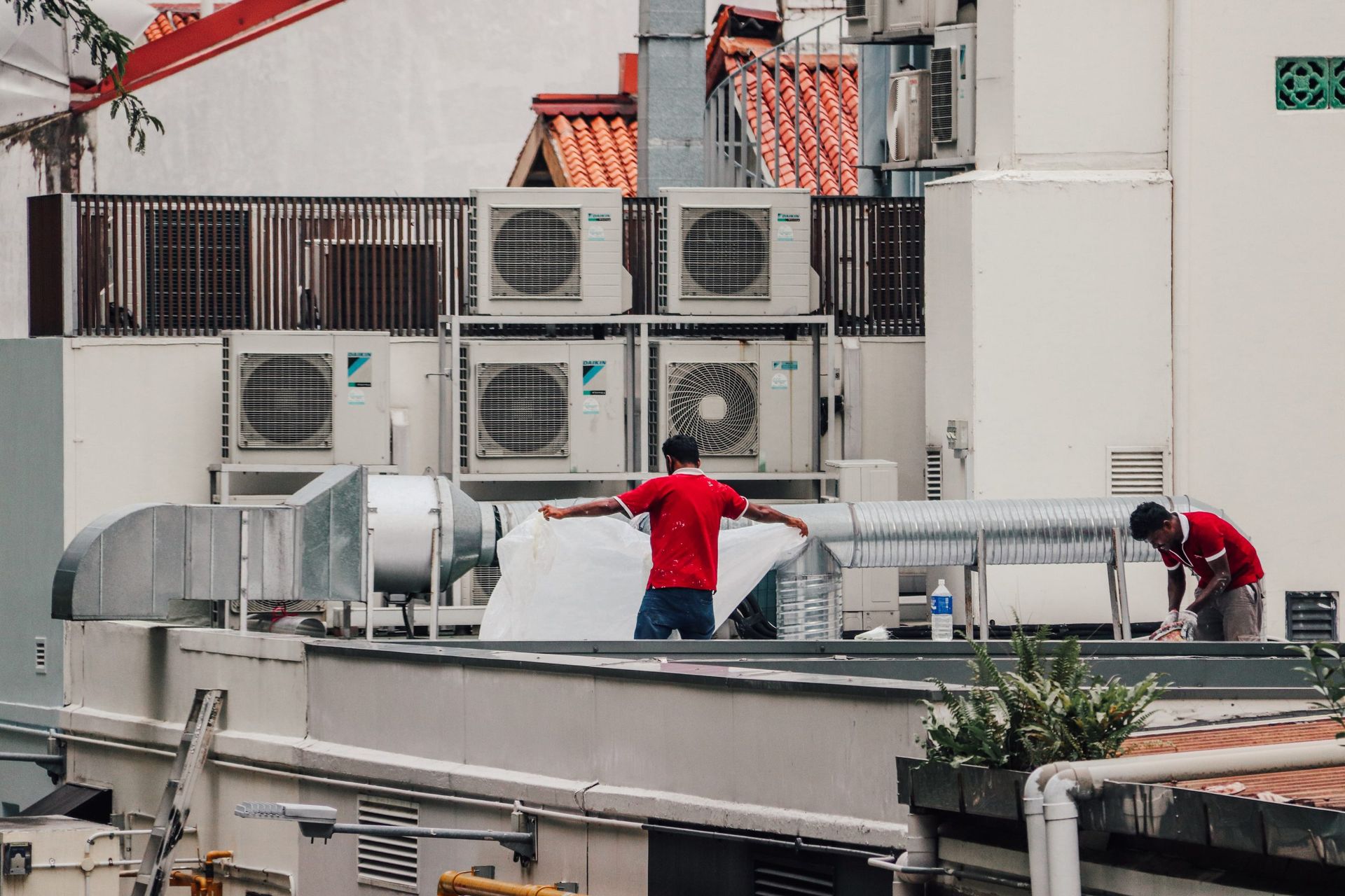 Two workers in red shirts on a building roof with air conditioning units. San Jose's Best Commercial HVAC Business.