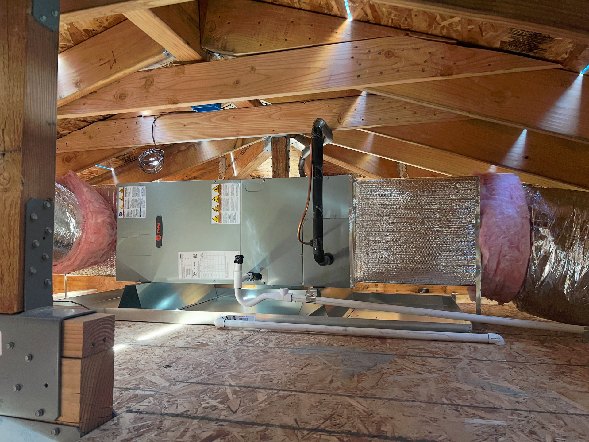 HVAC unit in an attic, surrounded by wooden beams and insulation.