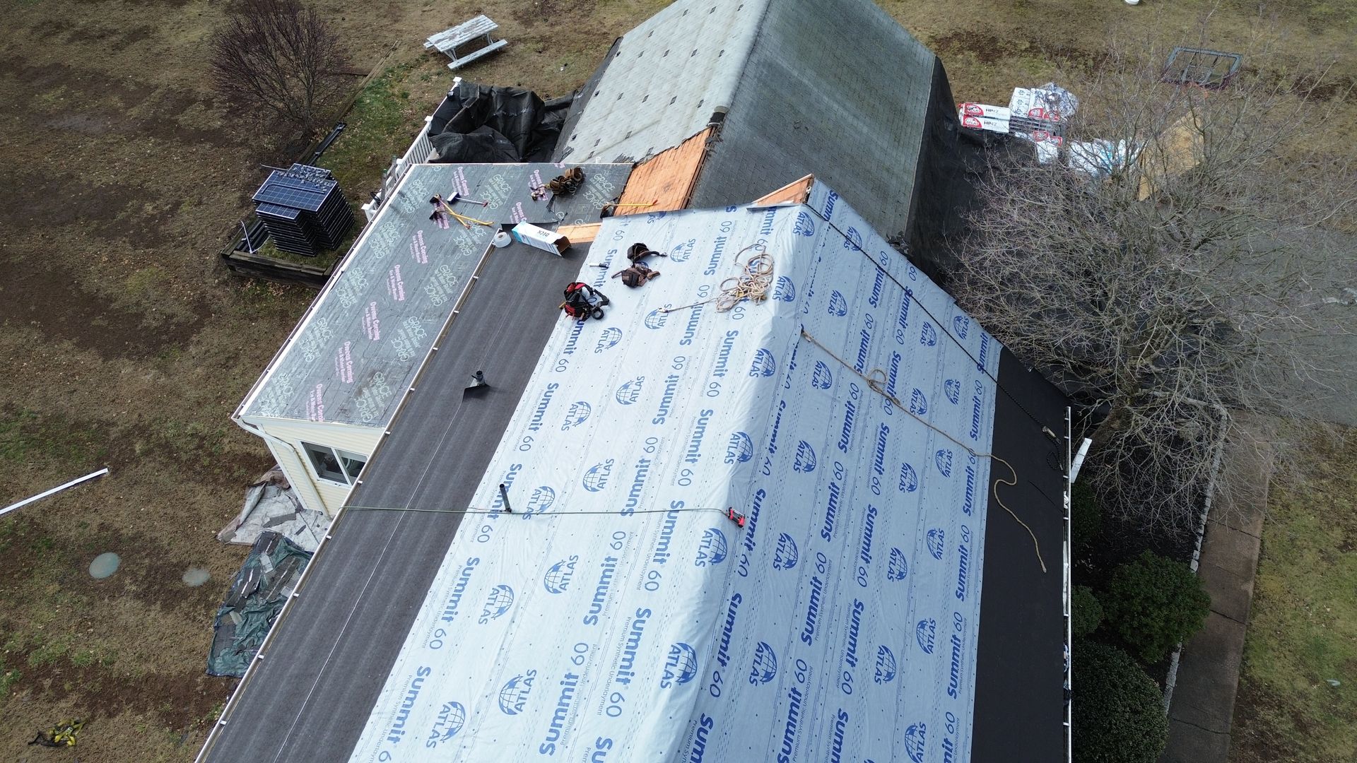 An aerial view shows workers installing synthetic underlayment on a residential roof during a renovation.
