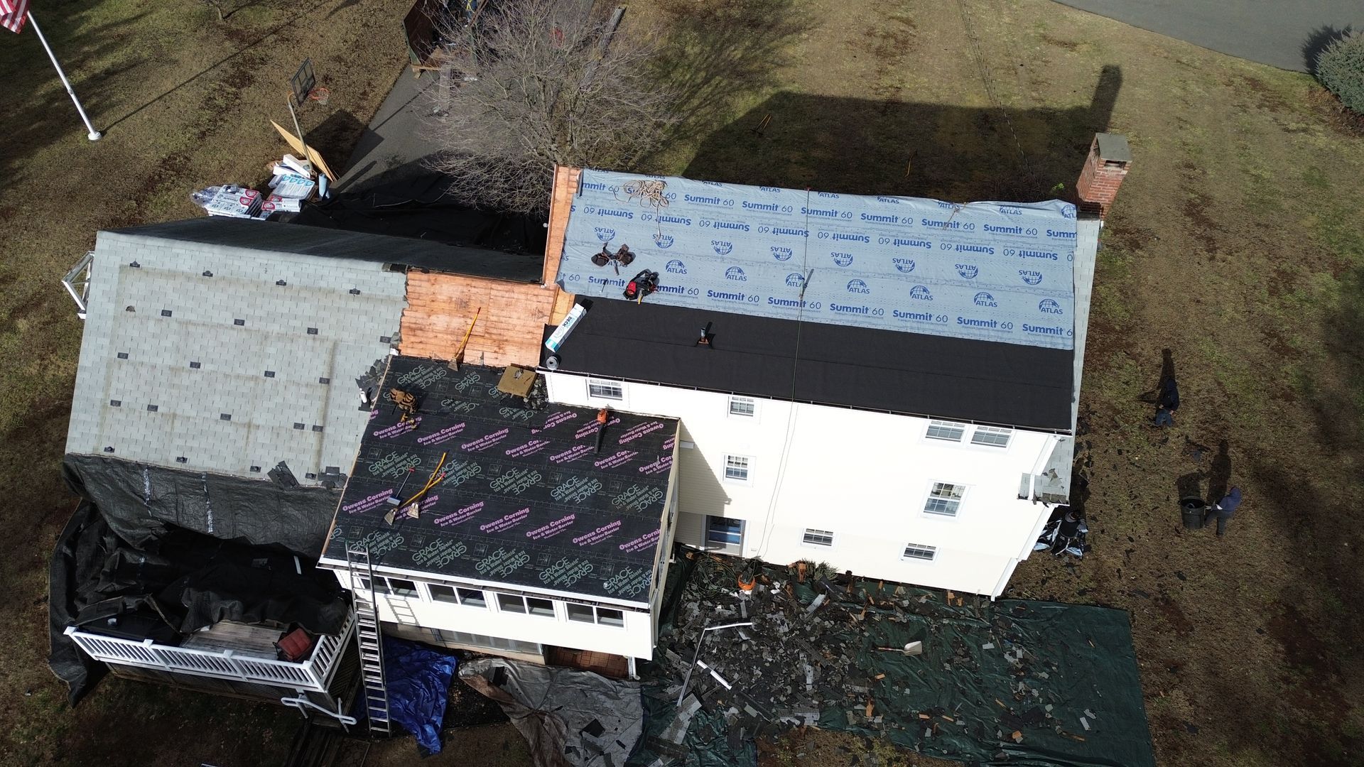 Aerial view of a house roof under construction, showing areas with new underlayment, bare plywood, and roofing material.