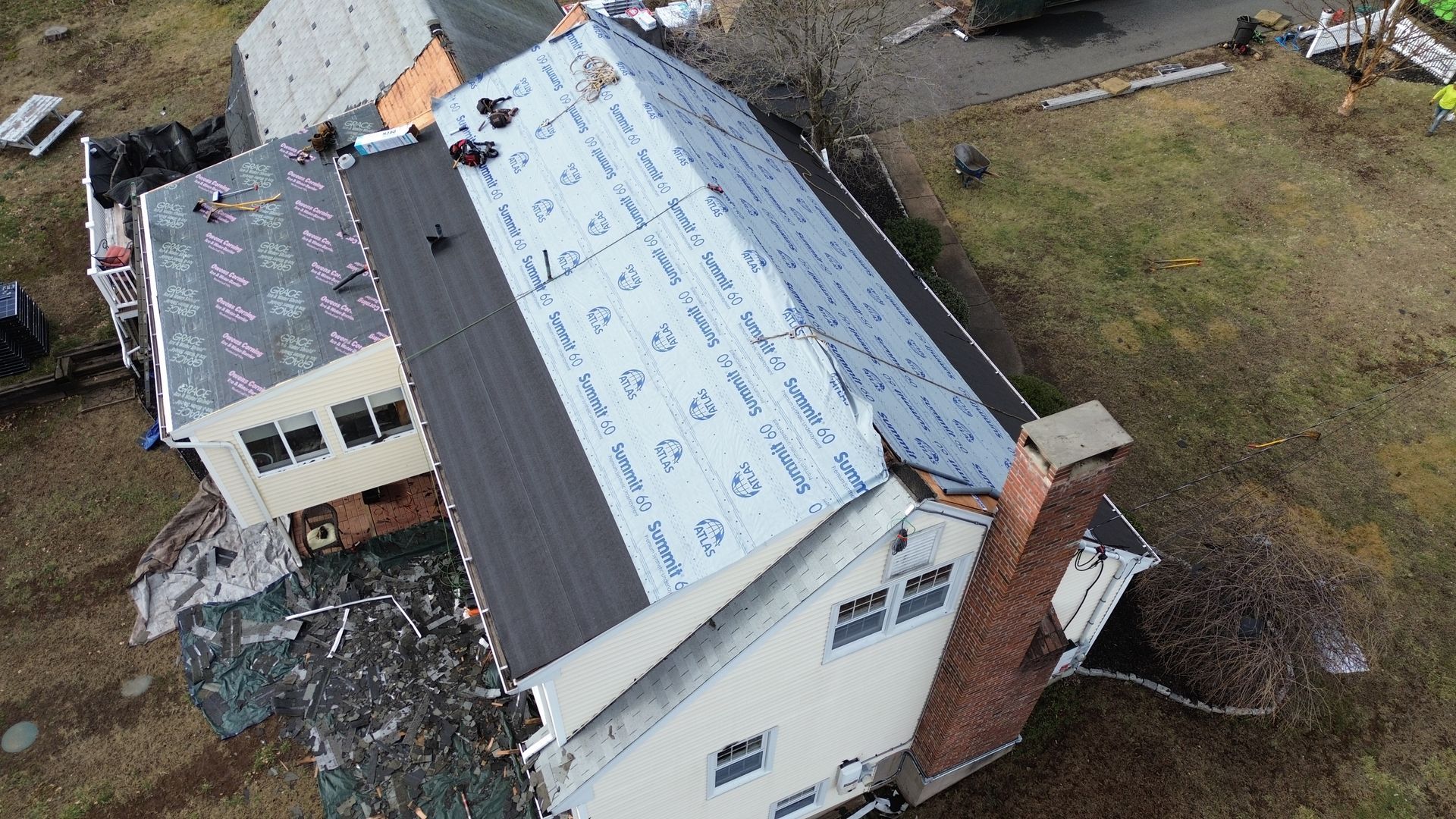 Aerial view of a house undergoing roof replacement with shingles and protective underlayment on the roof surface.