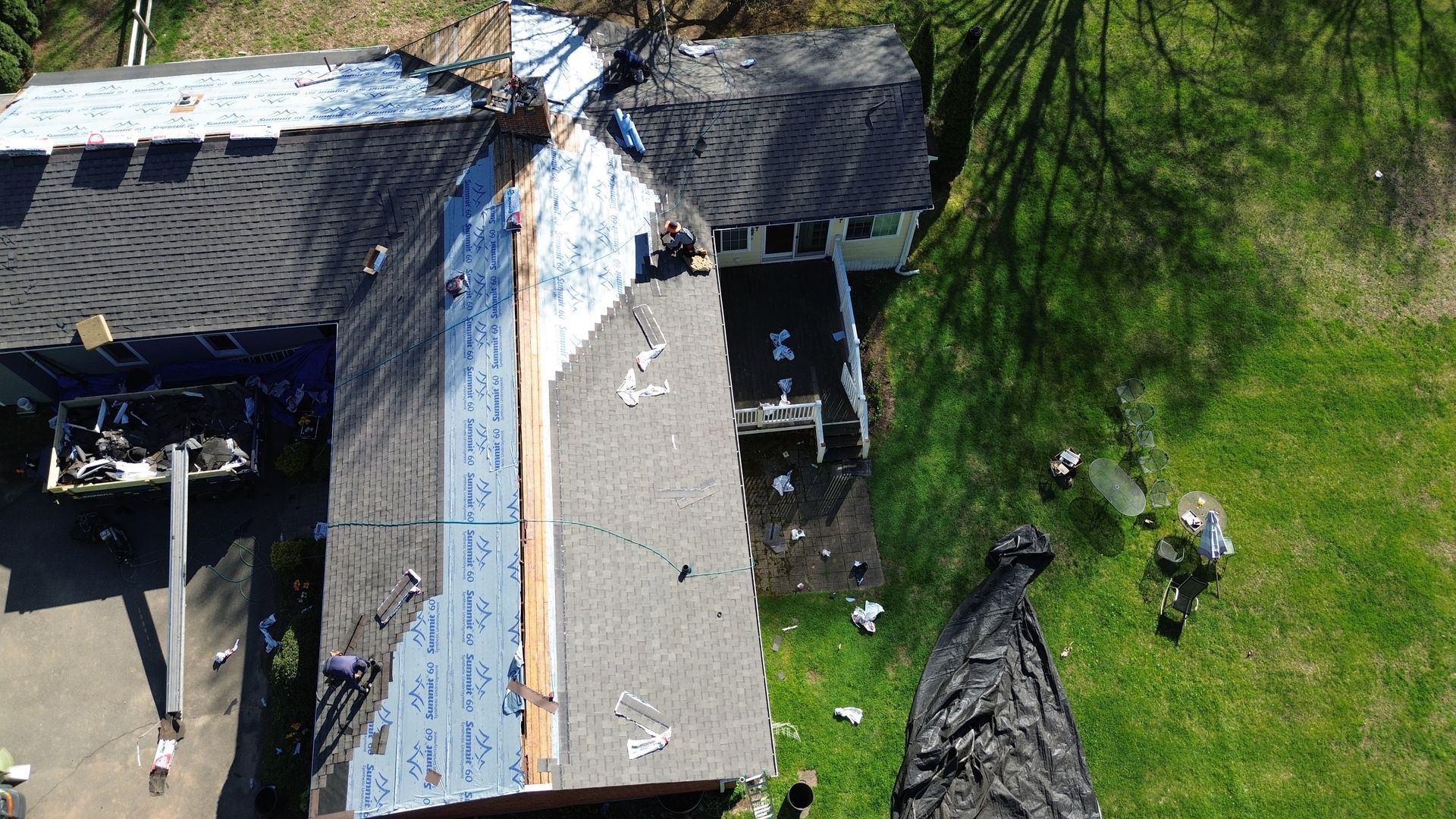 An aerial view of a house undergoing a roof replacement, with sections showing shingles, exposed underlayment, and debris.