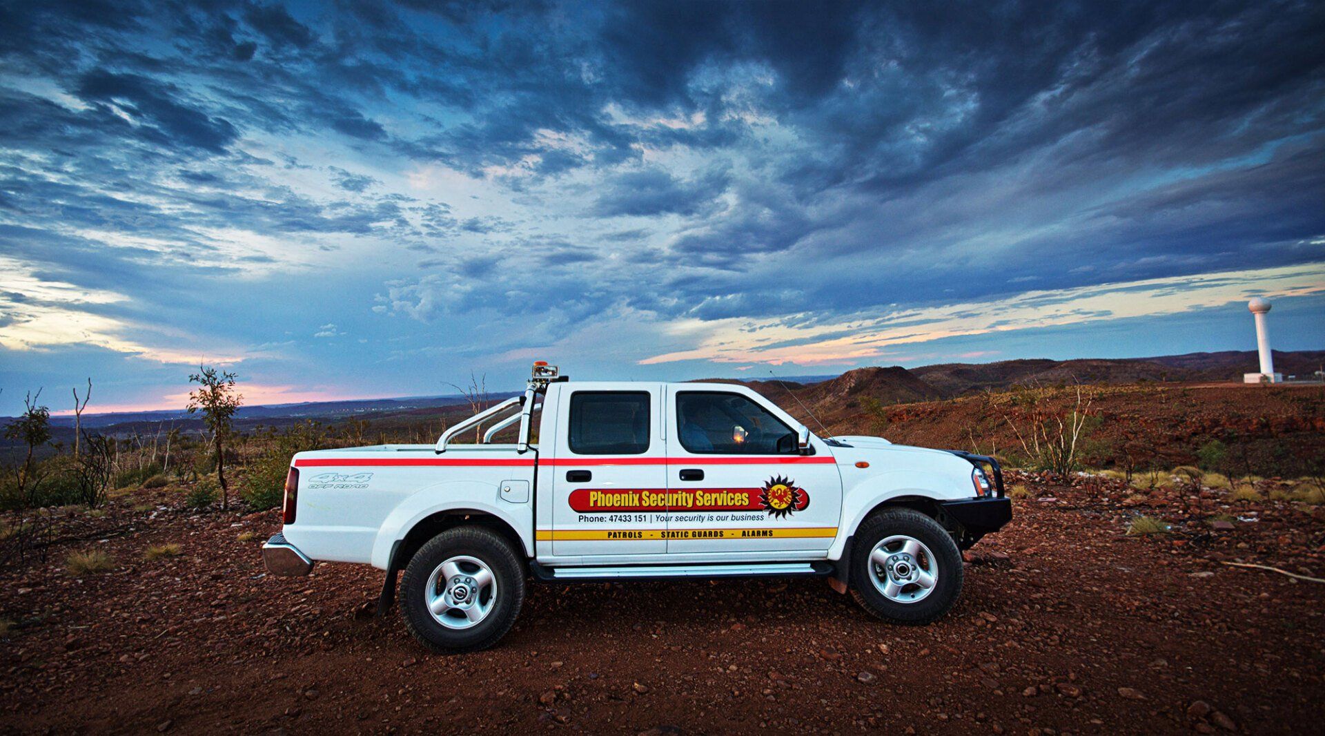 White pickup truck with company logo parked on dirt road, against a backdrop of a cloudy sky and arid landscape.