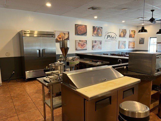 Interior of a commercial kitchen with stainless steel appliances, food preparation counter, and food images on the wall.