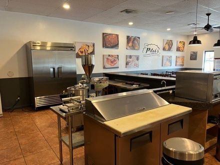 Interior of a restaurant kitchen, with stainless steel appliances and food photos on the wall.