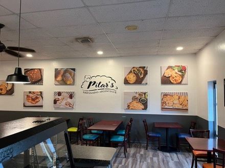 Interior of Pilar's restaurant with food photos, tables, and a logo on the wall.